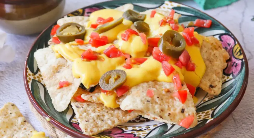 Nachos con queso derretido, jalapeños y tomate picado en un plato decorado.