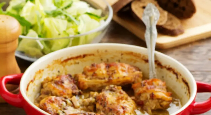 Pieczony królik w czerwonej naczyniu, z dodatkiem marynaty do królika pieczonego w piekarniku, podany z sałatką i chlebem.