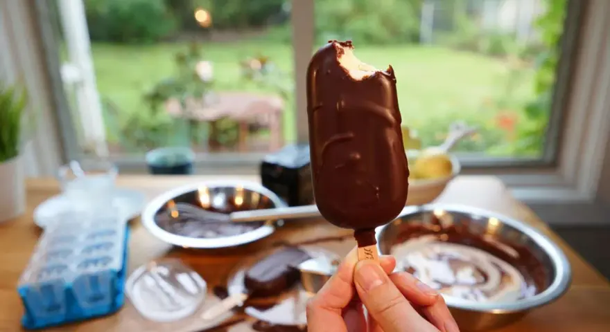 Ein abgebissener Schokoriegel, der zeigt, wie einfach es ist, Magnum Eis selber machen. Zutaten und Eisformen liegen bereit.
