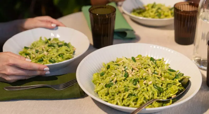 Due piatti di trofie al pesto, condite con fagiolini e pinoli, pronte per essere gustate.