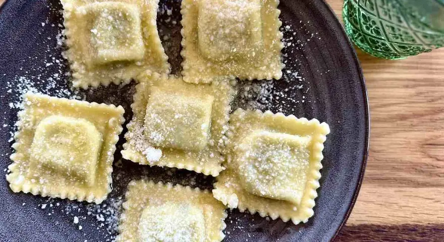 Pięć świeżych ravioli z ricottą i szpinakiem, posypanych parmezanem. Idealne do przygotowania według przepisu.