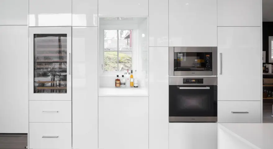 Cucina moderna bianca con elettrodomestici integrati e una porta finestra che offre una vista sul verde.
