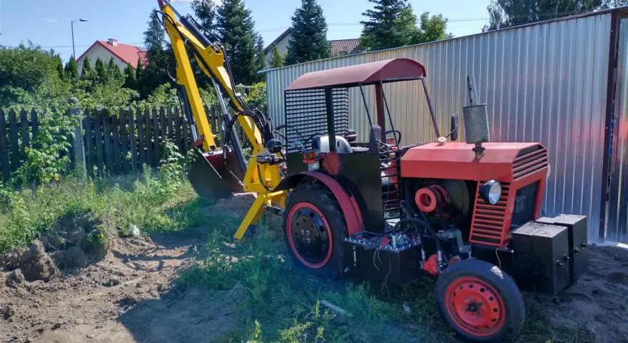 Czerwony traktor C-330 z zamontowaną żółtą koparką, gotowy do pracy w ogrodzie.