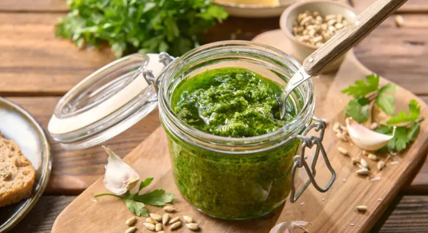 Słoik domowego pesto z pietruszki, z czosnkiem, nasionami słonecznika i serem w tle. Idealne do makaronu lub na grzanki.