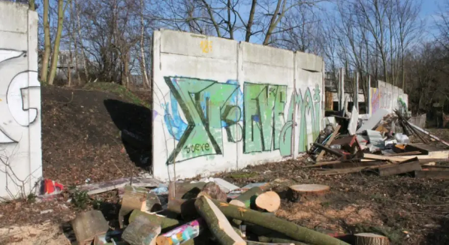 Graffiti-bemalte Überreste der Berliner Mauer, umgeben von Holzstapeln und Trümmern.