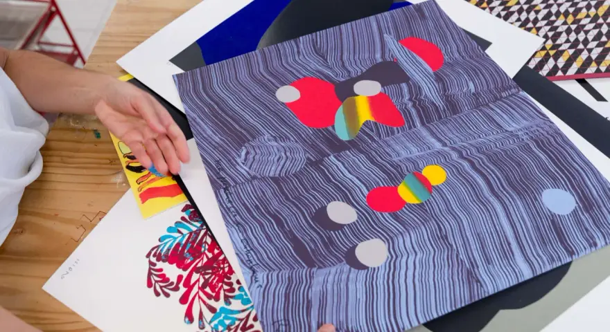 Manos revisando impresiones de arte abstracto, con vibrantes colores y patrones. El material serigrafia resalta en cada detalle.