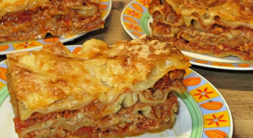 Prosty przepis na lasagne z mięsem mielonym. Aromatyczne, warstwowe danie z makaronem, sosem mięsnym i serem, podane na kolorowych talerzach.
