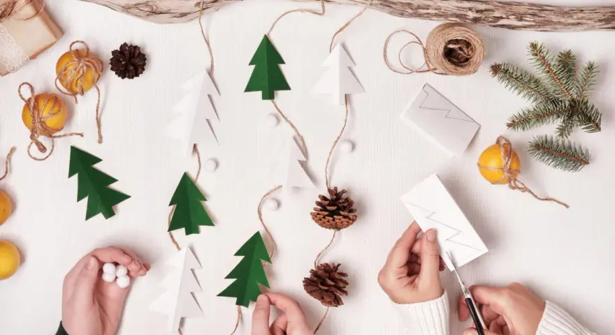 Kinder basteln Weihnachtsgeschenke: Papierbäume, Zapfen und Orangen werden zu einer festlichen Girlande.