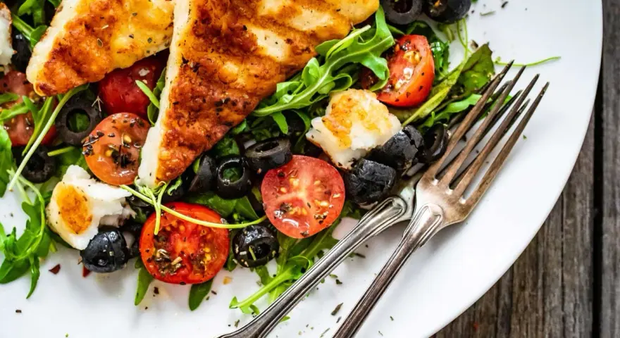 Pyszna sałatka z grillowanym halloumi, pomidorkami koktajlowymi i czarnymi oliwkami na talerzu.