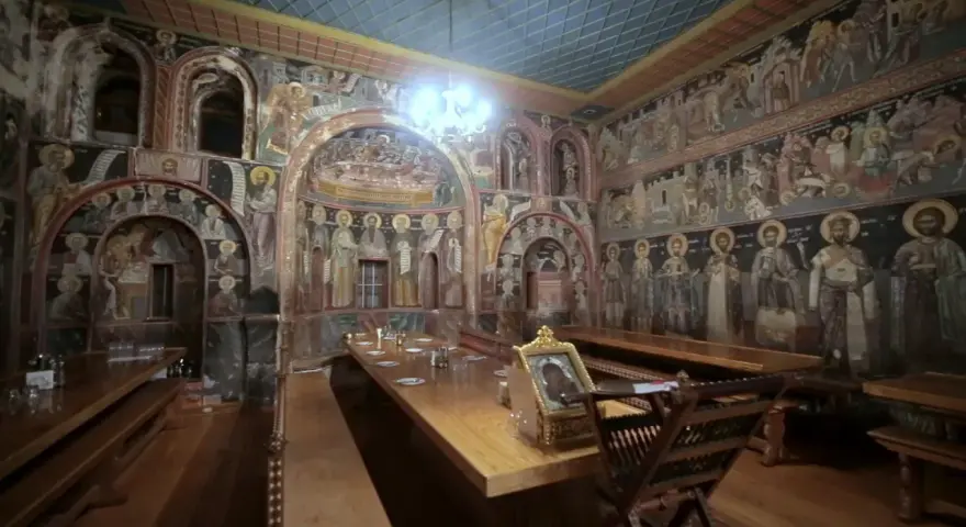 Inside Mount Athos, a refectory is adorned with ancient frescoes depicting religious scenes and figures.