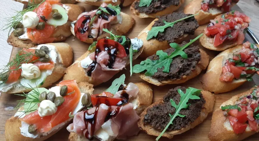 Pyszna przekąska na desce: bruschetty z łososiem, szynką, pomidorami i pastą oliwkową.