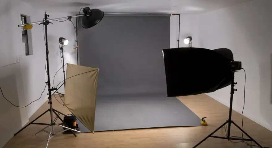 Studio fotograficzne z szarym tłem, lampami i dyfuzorem. Światło kontrowe tworzy dramatyczne cienie.