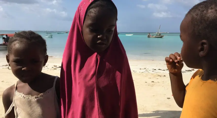 Dzieci na plaży, w tle turkusowe morze i łodzie. To obrazek z życia na Zanzibarze.
