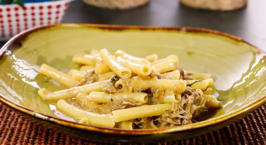 Piatto di ziti alla genovese, pasta condita con un ricco ragù di carne, servita in una ciotola verde.