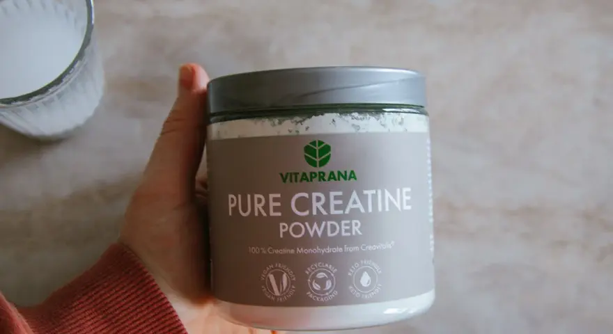 En hand håller en burk med Vitaprana Pure Creatine Powder. Kan vara ett komplement för den som vill ha **kreatin viktnedgång**.