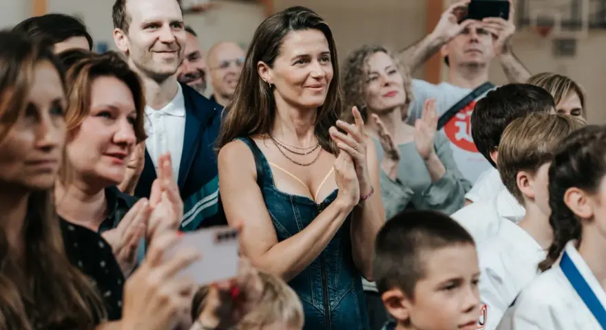 Agnieszka Grochowska z uśmiechem klaszcze, otoczona ludźmi na widowni.