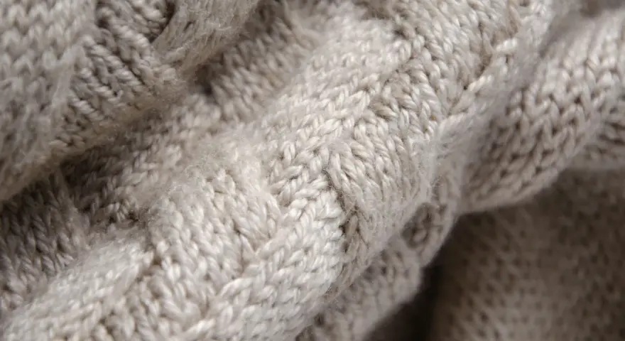 Tessuto a maglia grossa color crema, con un motivo a trecce che ricorda la morbidezza della flanella.