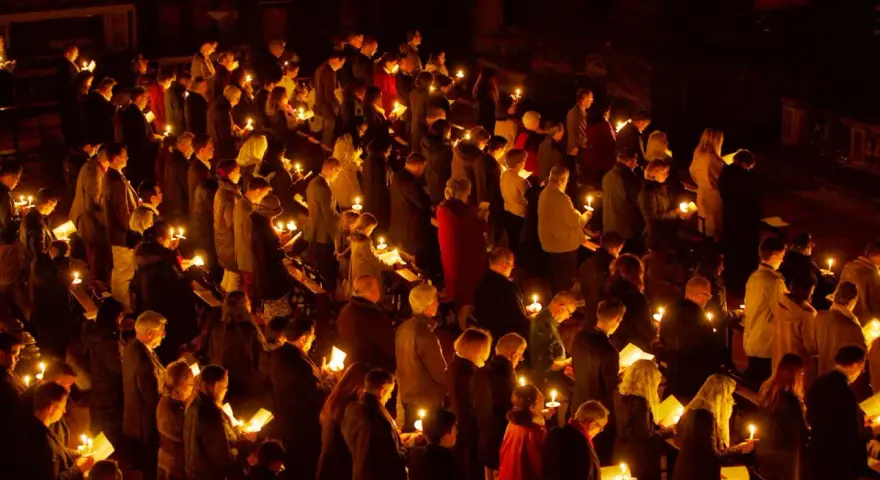 A solemn vigil unfolds as a congregation holds candles, their faces illuminated by the soft glow.