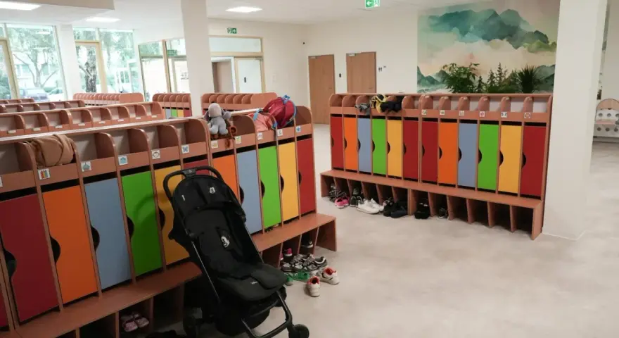 Kolorowe szafki i ławki w zespole szkolno-przedszkolnym, gotowe na przyjęcie dzieci. Wózek spacerowy czeka na swojego małego pasażera.