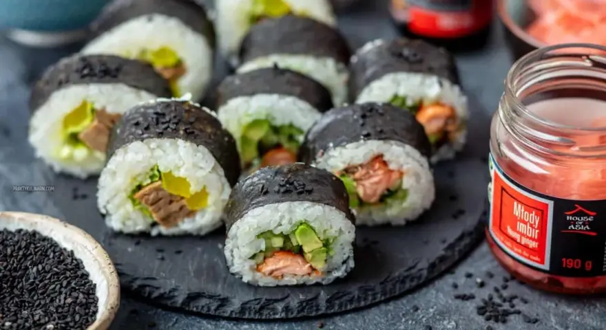 Gotowe sushi z łososiem i awokado, idealne do nauki jak zrobić sushi w domu. Obok słoiczek marynowanego imbiru.