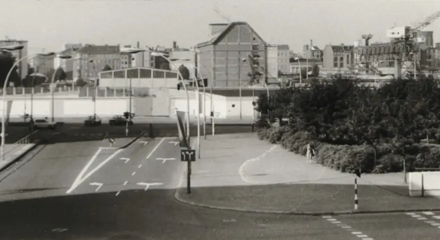 Straßenszene in Berlin der 80er Jahre mit Autos, Ampeln und einem Kran im Hintergrund.