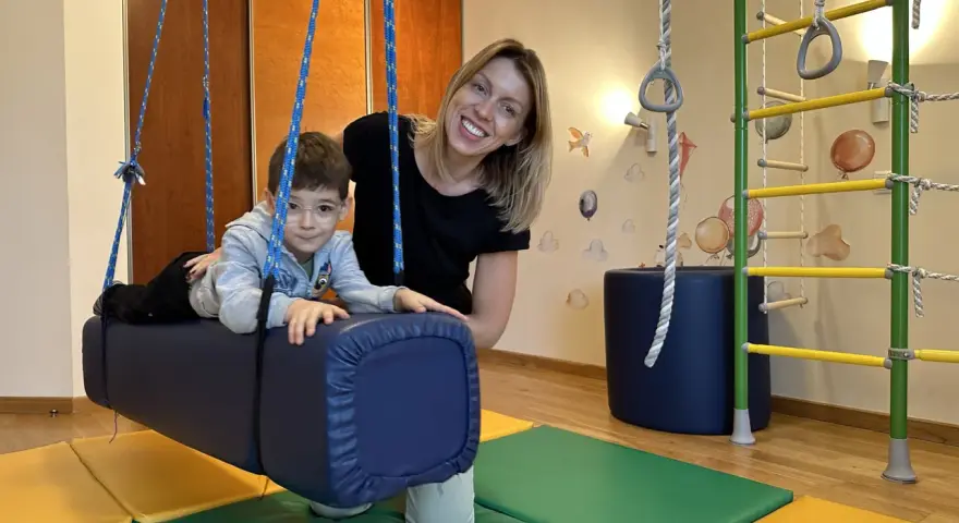 Chłopiec z ADHD u niemowlaka ćwiczy na huśtawce terapeutycznej z uśmiechniętą fizjoterapeutką.