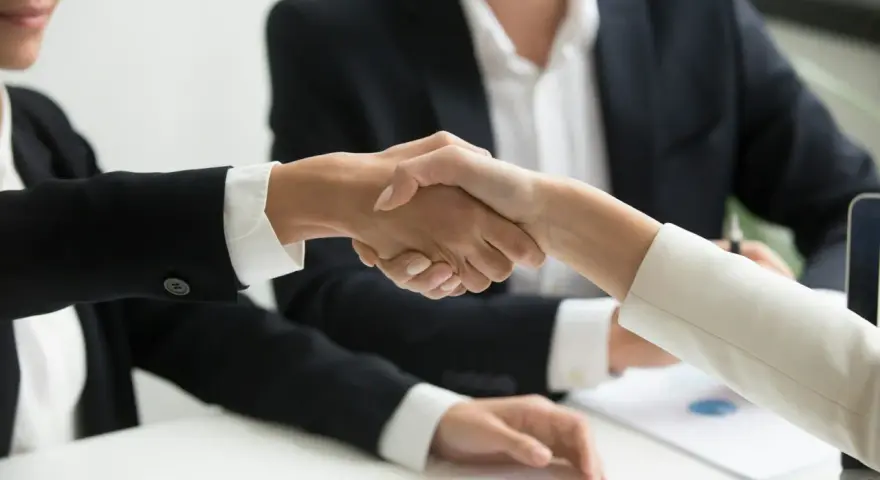 Poignée de main entre deux personnes en costume, symbolisant un accord ou un changement de dirigeant.