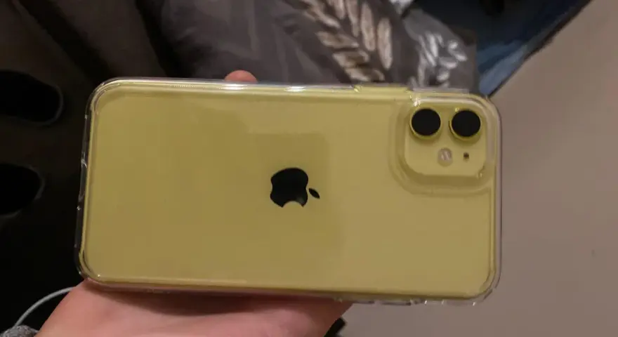 Żółty iPhone 11 w przezroczystym etui, trzymany w dłoni.