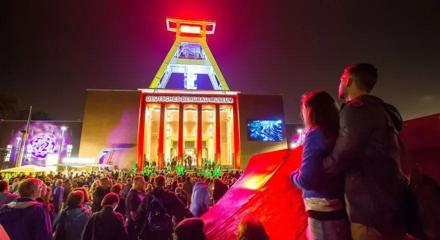 Ein Paar genießt die stimmungsvolle Nachtveranstaltung "Extraschicht Bochum" vor dem beleuchteten Deutschen Bergbau-Museum.