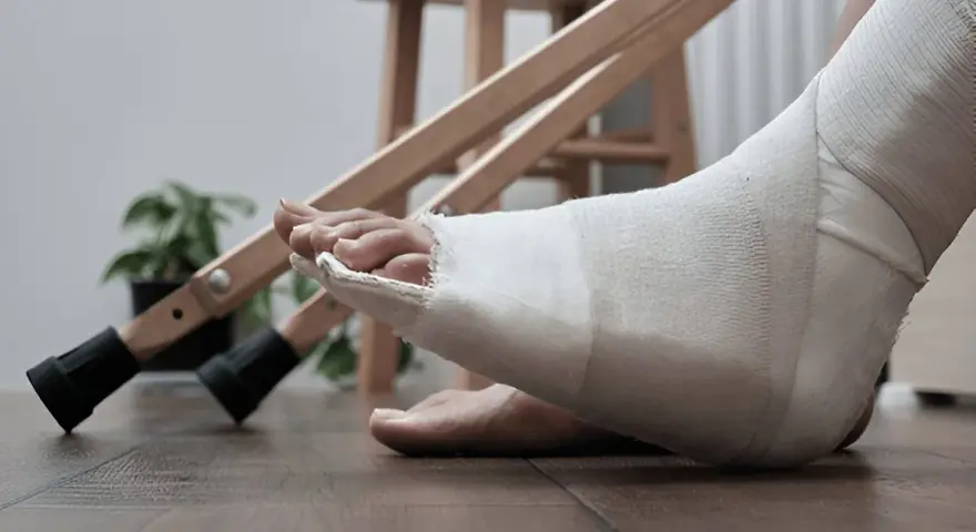 Noga w opatrunku, przygotowanie do rehabilitacji palca po złamaniu. Obok stoją kule.