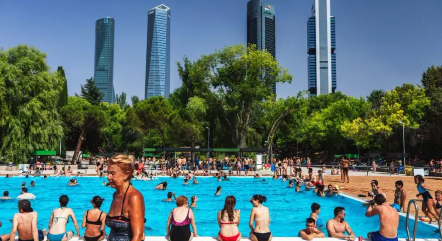 Gente disfrutando en una vibrante piscina comunitaria, con rascacielos modernos de fondo y árboles frondosos.