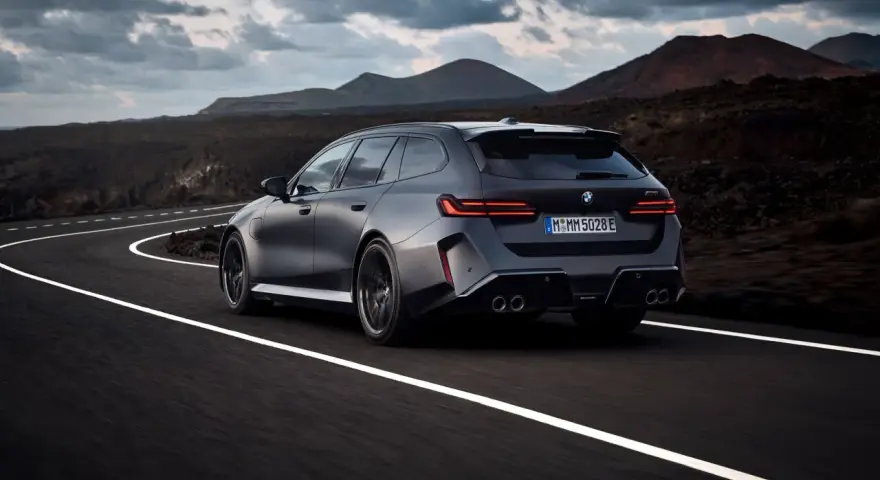 Mocne BMW M5 Touring pędzi po krętej drodze pośród surowego krajobrazu.