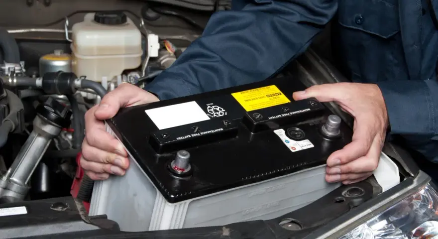 Mekaniker byter ett urladdat bilbatteri i motorutrymmet.