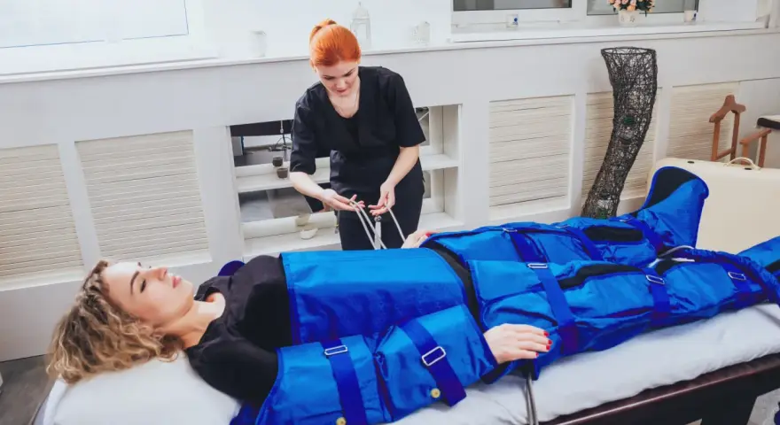 Kobieta w salonie piękności przechodzi zabieg drenażu limfatycznego. Terapeuta przygotowuje urządzenie do masażu uciskowego.
