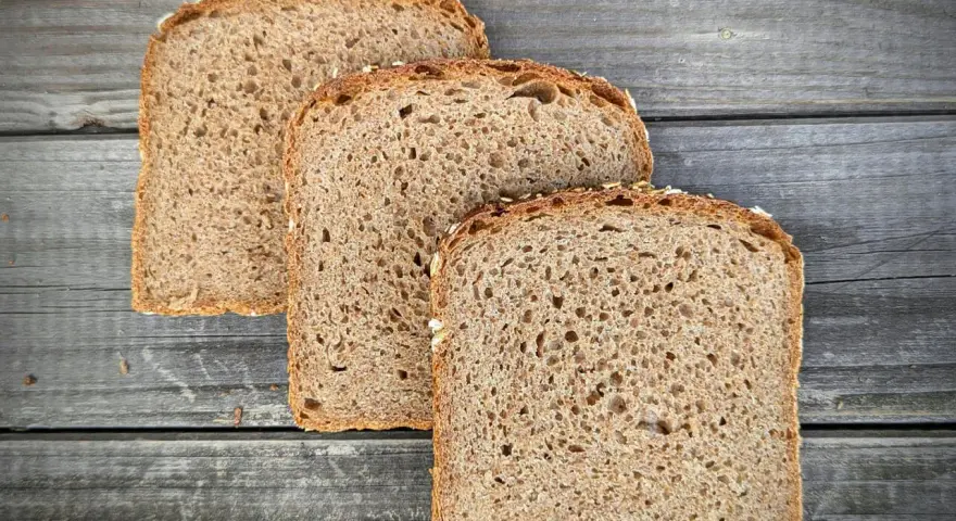 Drei Scheiben **Vollkornbrot** aus der **Kastenform** liegen auf rustikalem Holz.
