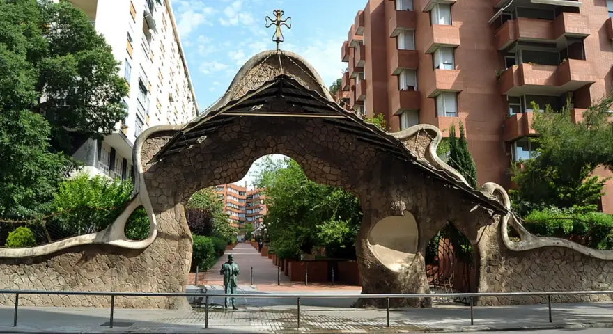 Portail organique, œuvre de Gaudí à Barcelone, avec une statue d'homme devant.