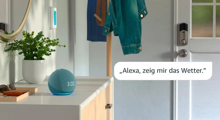 Alexa Routine erstellen: Ein blauer Echo Dot mit leuchtender Uhrzeit und eine Pflanze stehen auf einer Kommode. Eine Jacke hängt an einem Kleiderständer.
