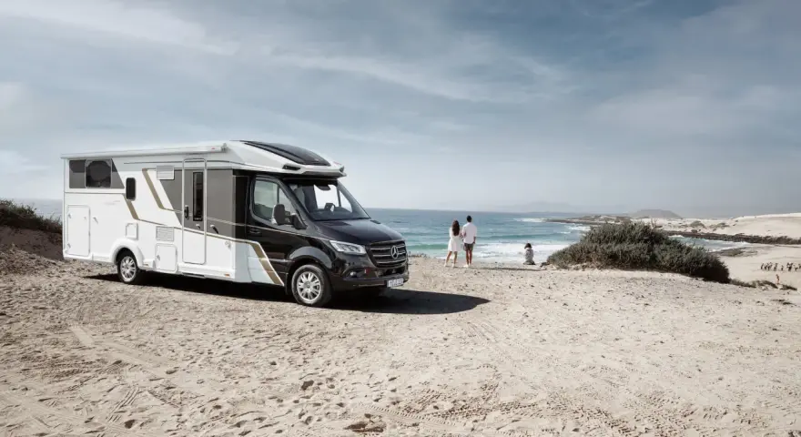 Eura Mobil husbil parkerad på en sandstrand vid havet. Ett par står och tittar ut över vågorna.
