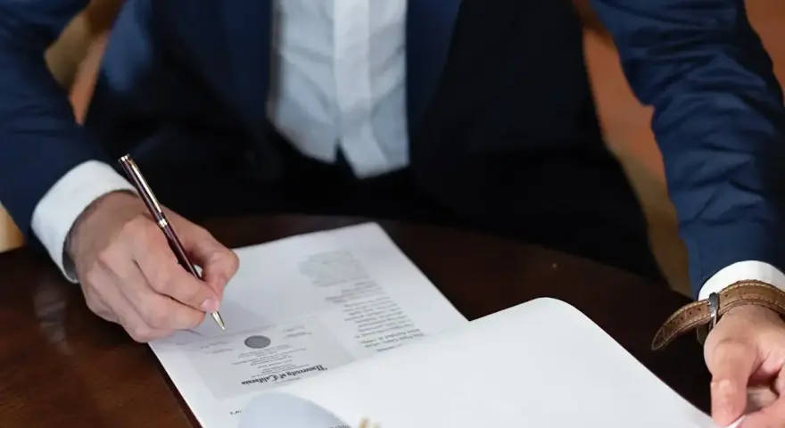 Mężczyzna w garniturze podpisuje dokument, składając oświadczenie woli.