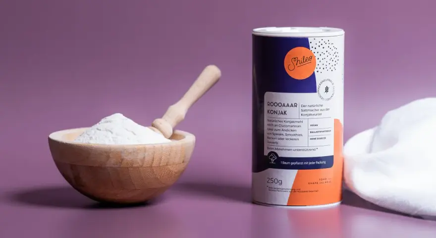 Holzschale mit weißem Konjakmehl und Löffel daneben, eine Dose mit der Aufschrift "Konjakmehl" und Produktinformationen.
