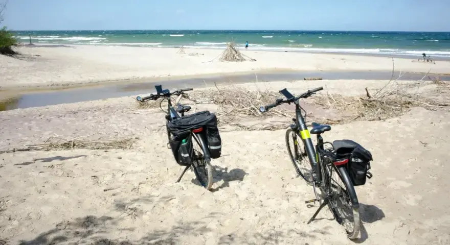 Dwa rowery z sakwami na piaszczystej plaży, gotowe na odkrywanie tras rowerowych nad morzem.