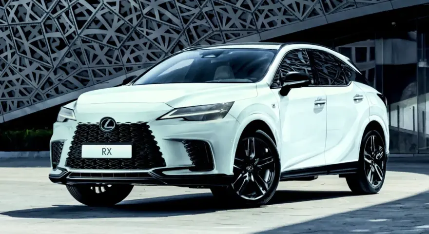 Biały Lexus RX500h z czarnymi felgami stoi przed nowoczesnym budynkiem o geometrycznej fasadzie.