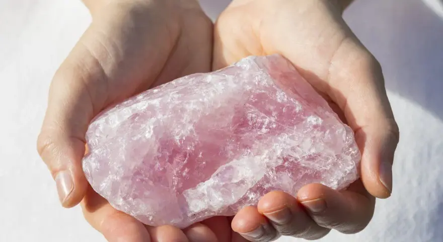 Manos sostienen una gran piedra de cuarzo rosa, una piedra para la salud y el bienestar, con su translúcida belleza.