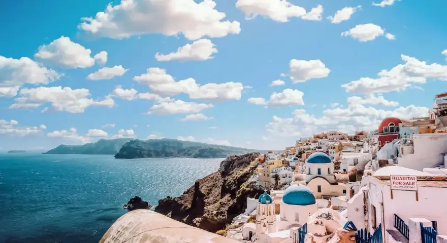 Santorini, Grecja. Ile się leci do raju? Białe domki z niebieskimi kopułami na tle błękitnego morza i nieba.