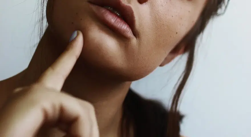 A woman's face, with a finger gently touching her cheek, suggesting a moment of self-care and a relaxing facial massage at home.
