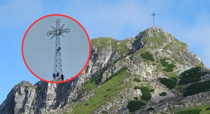 Ludzie wspinają się na krzyż na Giewoncie. Czy krzyż na Giewoncie świeci? Widać go z daleka na tle błękitnego nieba.