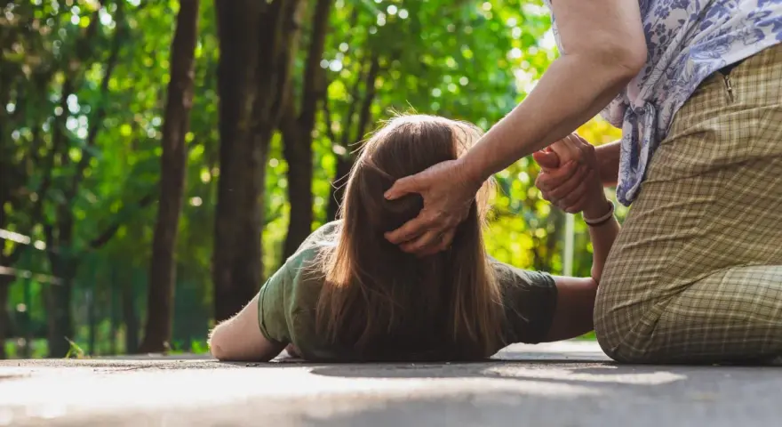 Osoba na ziemi, pomagająca jej druga osoba. Czy padaczka jest uleczalna? Ta scena budzi pytania o zdrowie i wsparcie.
