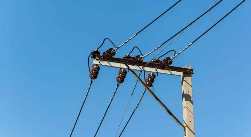 Słupy energetyczne z izolatorami ceramicznymi i przewodami pod napięciem. Brak zgody na służebność przesyłu może oznaczać problemy z infrastrukturą.