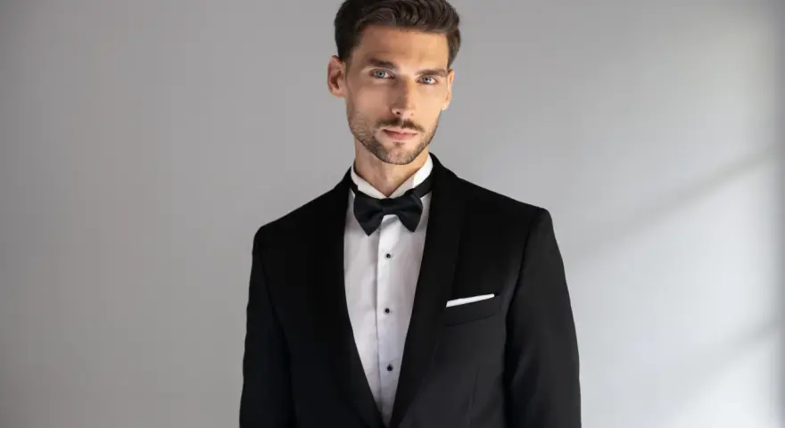 Elegancki mężczyzna w czarnym smokingu z białą poszetką. Dowiedz się, jak dobrać poszetkę do stylizacji.