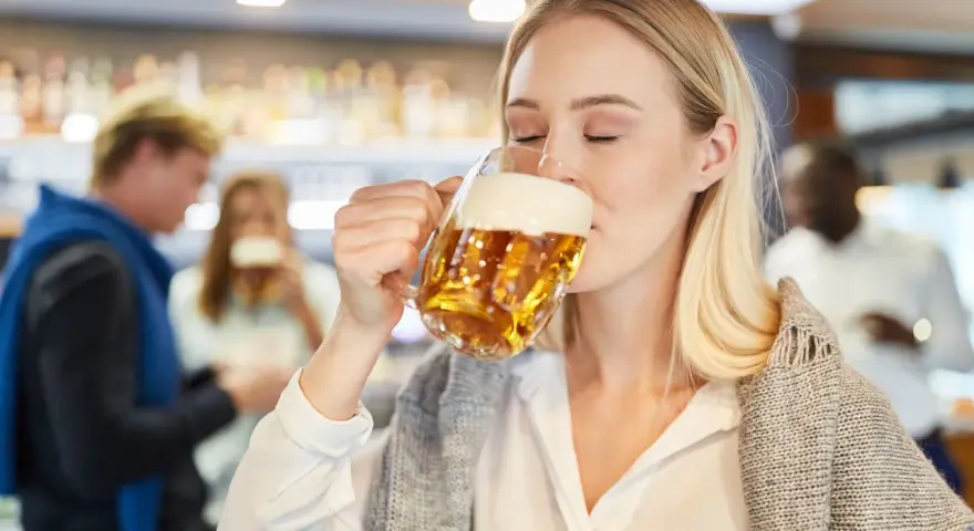 Kobieta z zamkniętymi oczami pije piwo bezalkoholowe w ciąży, ciesząc się smakiem w pubie.